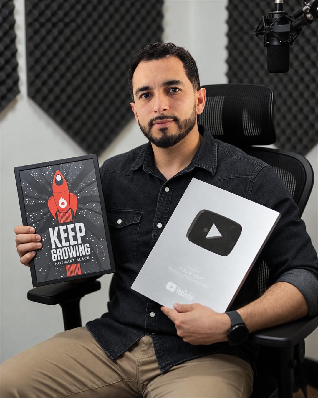 Cristian Parra Gaviria en su estudio, sosteniendo la placa Keep Growing de Hotmart Black y el Play Button de YouTube